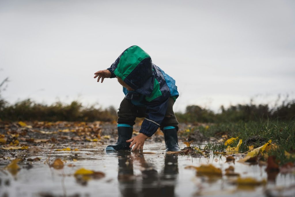 Jeune enfant en combinaison de pluie et bottes accroupi dans une flaque d'automne